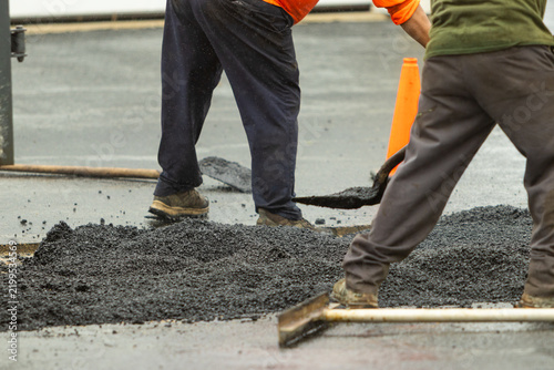 Two construction workers moving asphalt with shovels. 