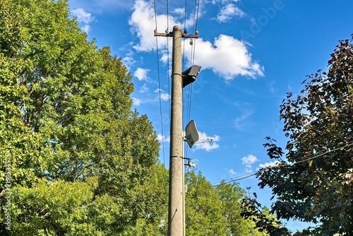 Obraz na plátně Concrete power utility pole with electric wires, public address loudspeaker, and satellite TV dish mounted against a blue sky with white clouds