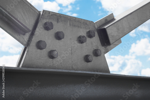 Fotografía Close-up of a heavy-duty galvanized steel structure joint with bolts and a gusset plate against a bright blue sky with clouds