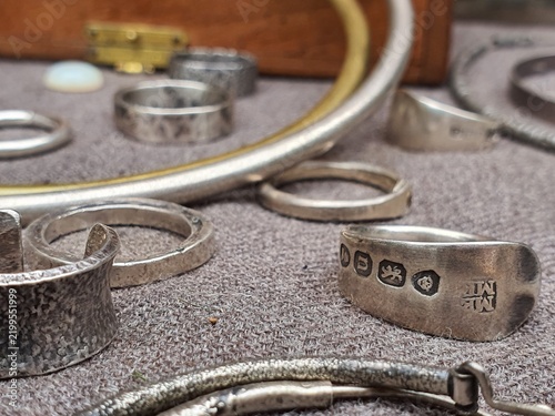 Close-up macro photograph of sterling silver rings displaying British hallmark stamps, arranged on a grey felt-lined surface. The image prominently features a vintage silver band in sharp focus