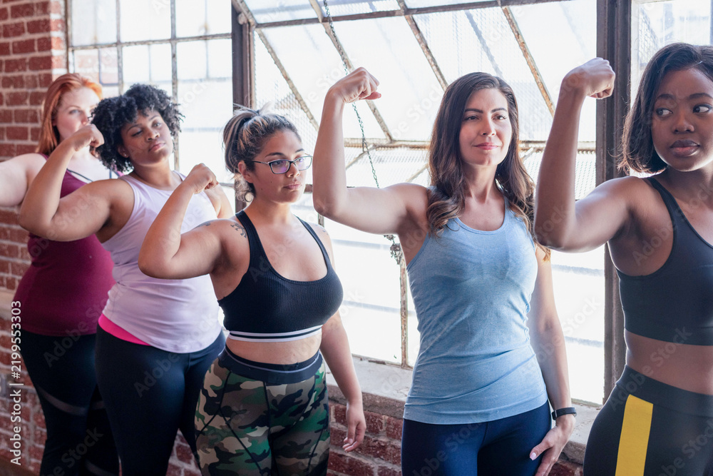 Fototapeta premium Diverse women flexing biceps in a bright studio, confident fitness pose