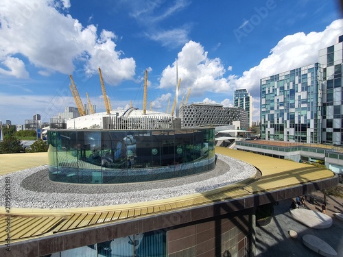 A panoramic view of modern architecture on the Greenwich Peninsula in London, UK, featuring the iconic O2 Arena (Millennium Dome) with its distinctive white tensile dome and yellow support towers