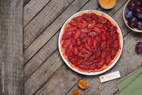 Plum tart on shortcrust pastry on a ceramic plate against a gray wooden background. Plum recipes.