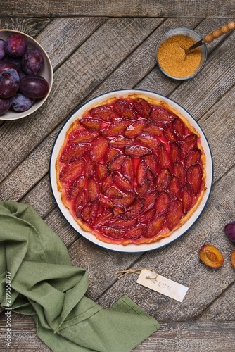 Plum tart on shortcrust pastry on a ceramic plate against a gray wooden background. Plum recipes.