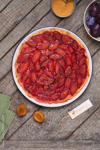 Plum tart on shortcrust pastry on a ceramic plate against a gray wooden background. Plum recipes.