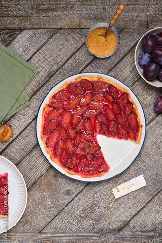 Plum tart on shortcrust pastry on a ceramic plate against a gray wooden background. Plum recipes.