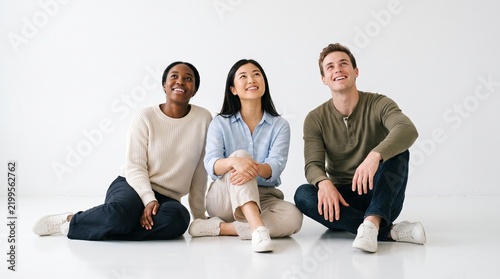 Diverse group of young adults sitting on floor looking up with smiles and hopeful expressions