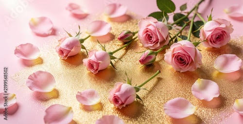 Pink rose blooms and petals scatter across gold glitter surface. Fresh roses with green stem rest on soft pink background. Romantic floral arrangement symbolizes beauty and love.