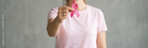 Breast Cancer Awareness Month Woman in pink t-shirt holding pink ribbon in front of grey breast cancer awareness