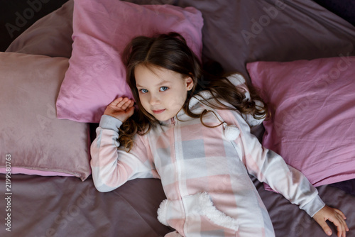 Girl in Plush Pajamas Lying on Bed Among Pink Pillows Top View