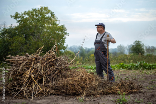 Fotografía Field worker stands beside haylike pile holding shovel