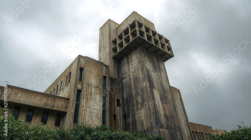Modern architecture. Monumental brutalist building with a tall concrete tower, geometric facade and cantilevered structure under a cloudy sky.