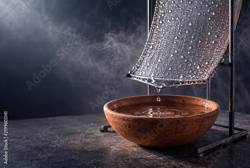 Water dripping from a metal mesh panel into a terracotta bowl
