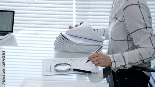 Professional woman categorizing important business documents and financial statements on an office desk. Managing a stack of files during a detailed audit