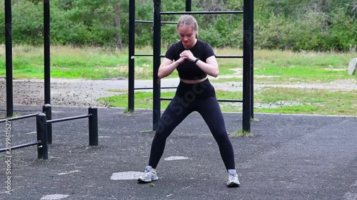 Fit young woman doing squats on an outdoor sports ground, lower body strength training, toned legs, active lifestyle, fitness concept