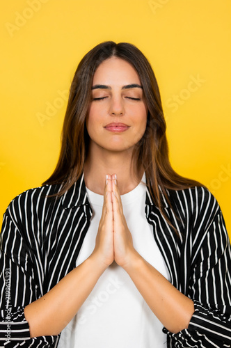 Fotografie Young woman with eyes closed and hands joined in prayer, practicing mindfulness