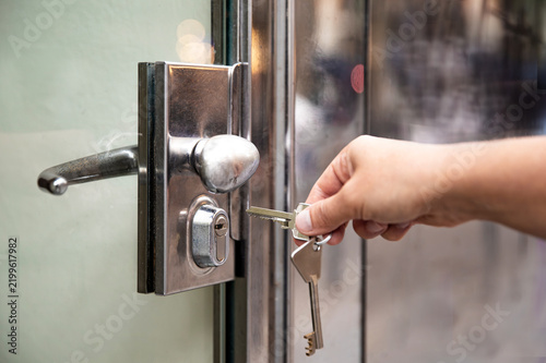 Opening a door with a key. Human hand inserting a metal key into the lock cylinder of a glass door