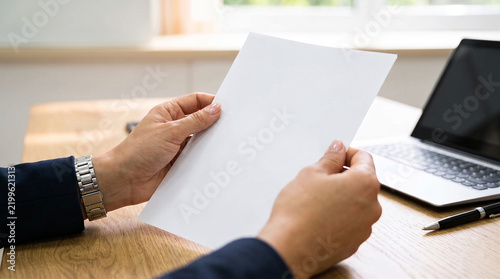 Professional person holding a blank white paper document at a desk with a laptop and copy space