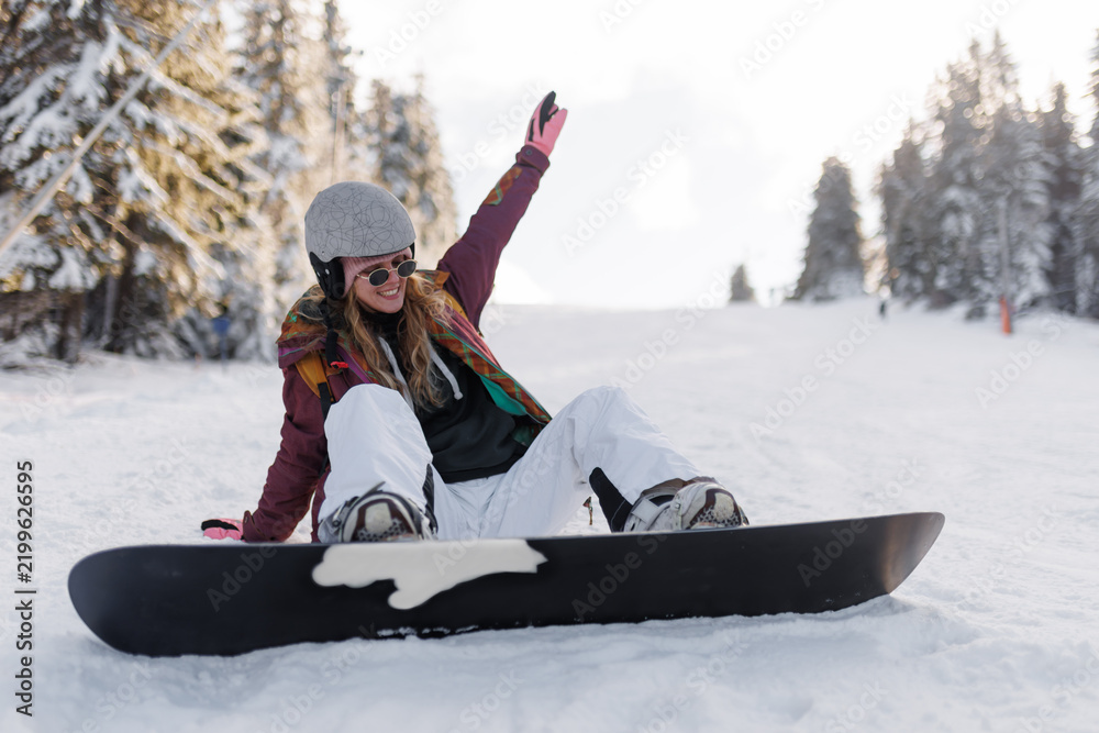 Fototapeta premium Girl snowboarding on a snowy slope while wearing a helmet and colorful jacket during a sunny day in a winter resort