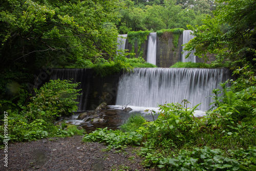Waterfalls over manmade concrete dams in lush green forest