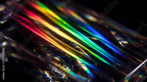 Abstract macro shot featuring vibrant light refraction through a glass prism creating a beautiful rainbow spectrum with streaks of red orange yellow green and blue against a dark background.