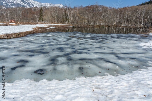 池の水面に残った氷と周辺に残る雪
