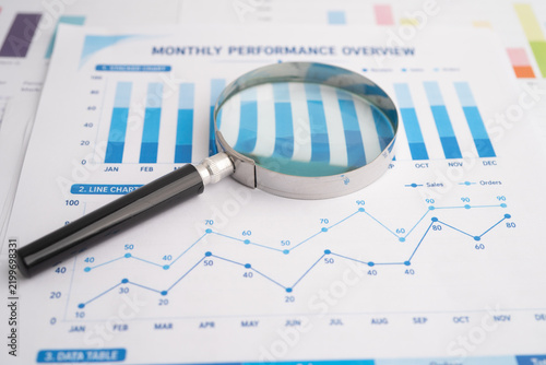 Magnifying glass on spreadsheet and graph paper.