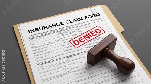 Insurance claim form with a wooden rubber stamp and a red denied ink imprint on gray background with document