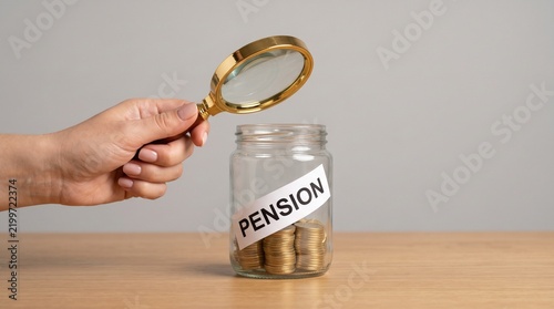 A hand holding a magnifying glass over a glass jar containing coins labeled with the word pension with wealth