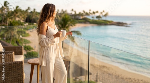 Woman drinking coffee on luxury balcony overlooking tropical ocean