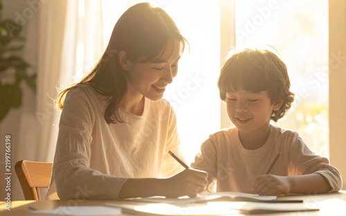 madre ayuda a un niño con sus tareas escolares mientras la luz cálida del atardecer ilumina el hogar. Concepto de educación, aprendizaje, acompañamiento familiar y vida cotidiana.