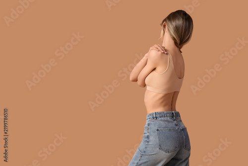 Young woman in stylish blue jeans posing on beige background, back view