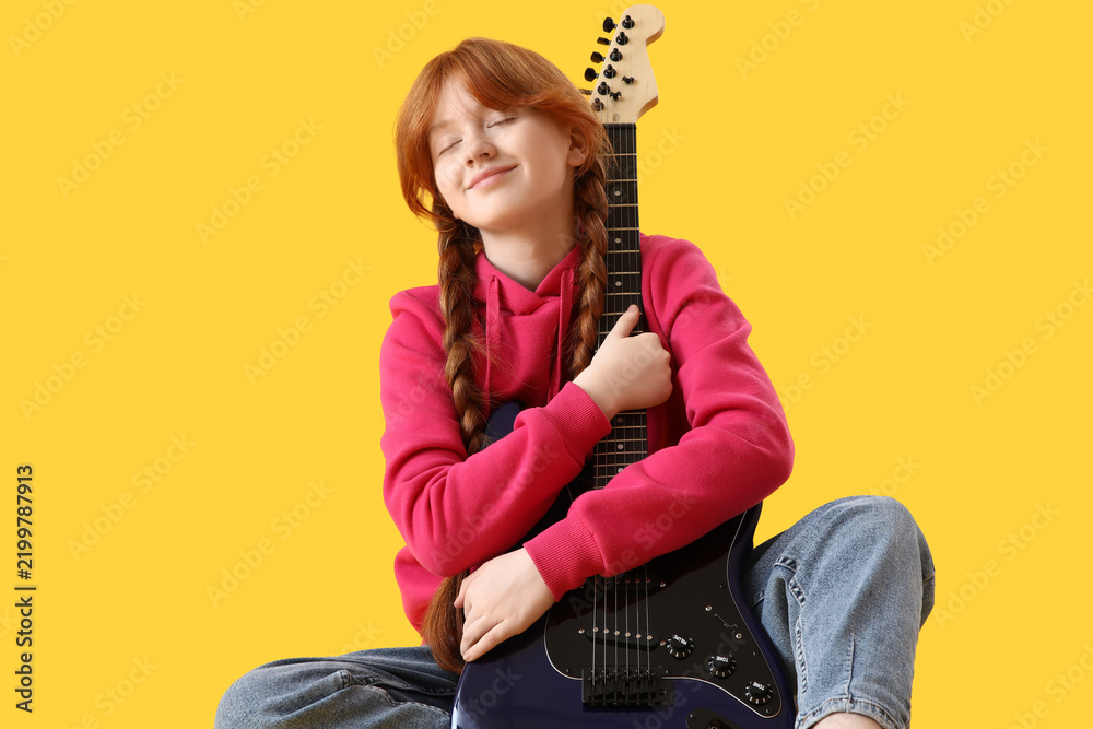 Fototapeta premium Redhead teenage girl hugging guitar on yellow background