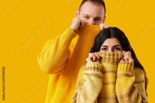 Young couple in warm sweaters on yellow background
