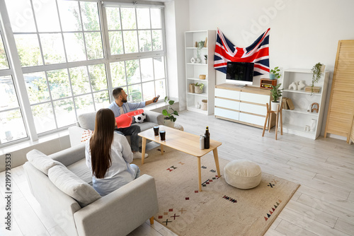 Young couple with UK flag watching football at home