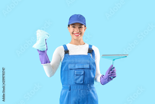 Female janitor with rag and squeegee on blue background