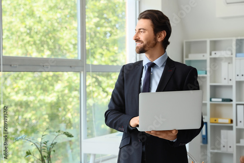 Young male secretary working with laptop in office