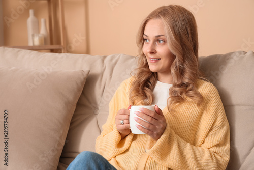 Beautiful blonde woman with tea cup sitting on sofa at home