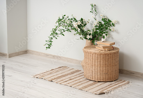 Wicker vase of blooming jasmine flowers and books on table near grey wall in ...