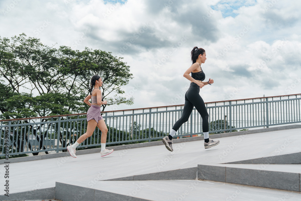 Obraz premium Two Asian women running outdoors on bridge for fitness and healthy lifestyle