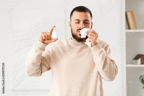 Sick young man with tissue and nasal drops suffering from allergy at home