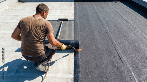 Professional roofer installing bituminous waterproof membrane on flat roof using gas torch for sealing