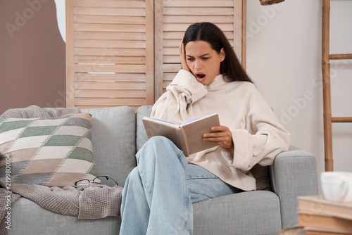 Beautiful young shocked woman reading book on sofa at home