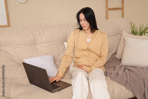 Young pregnant woman using laptop on sofa at home