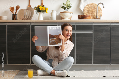 Young woman reading magazine on floor in kitchen