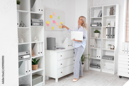 Beautiful businesswoman working with laptop near peg board in office