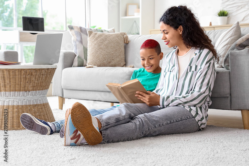 Little African-American boy with his mother reading book at home