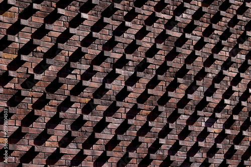 A sunlit brick wall with projecting bricks creating a pattern of contrasting light and shadow.