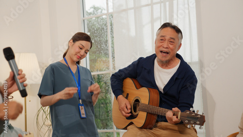 Fotografie Senior retirement nursing home music activity with caregiver and guitar, happy g