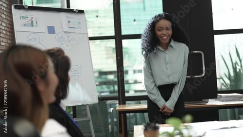 Smiling businesswoman giving presentation to colleagues in modern office, discussing business strategy, charts and project results during professional team meeting and corporate collaboration.